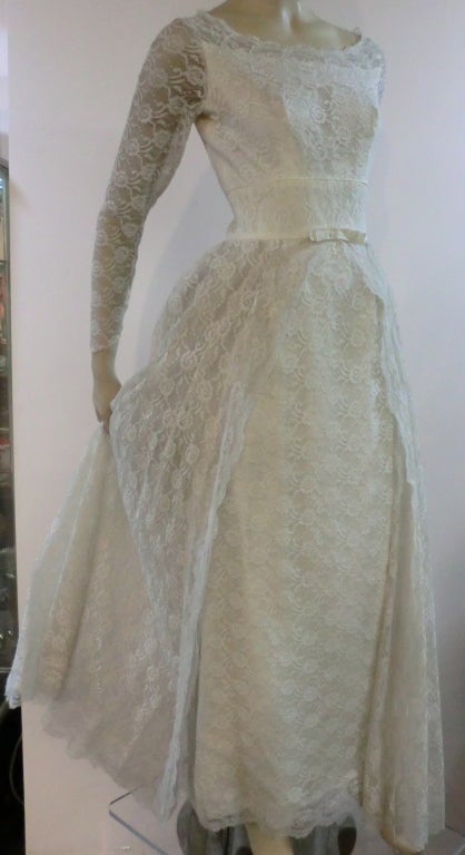 A wonderfully charming 50s white lace wedding gown straight out of a storybook.  With demure bateau neckline, long sheer sleeves, column skirt with a voluminous trailing overskirt.  Beautiful.  Size 4