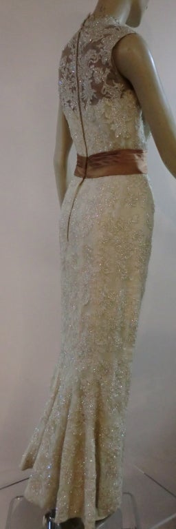 A gorgeous 60s lace gown for bride or special occasion.  Sleeveless, faux Mandarin collar,  sheer illusion back, cummerbund waistband and fishtail flare at hem in back.  Slim, sleek silhouette from the front.  Entire lace gown is embellished with