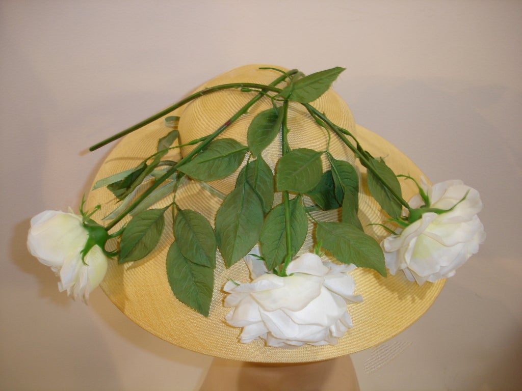 A gorgeous 1950s Leslie James straw wide-brimmed hat with3 large white artificial roses draped over the top.  Labeled Leslie James.  Measures  21.5