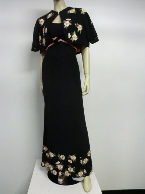 A fantastic black wool Enid Morris 60s Empire waist gown with bolero jacket to match.  Gown is trimmed at waist to silk velvet waist bands emphasizing a very low dipping back.  Bolero jacket and hem line of gown are embroidered with pink and green