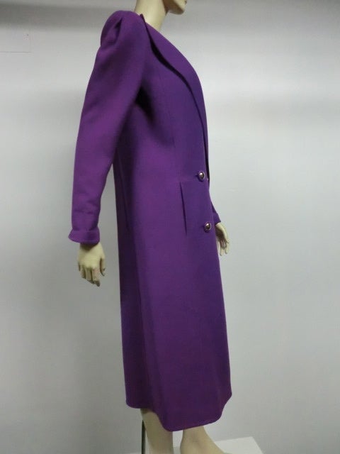 A Pauline Trigere purple wool coat from the 70s or early 80s: Double breasted with shoulder emphasis and silver and fabric buttons.  Narrow sleeves and a straight hipped silhouette. Side slash pockets. Never worn with original tags. Originally sold