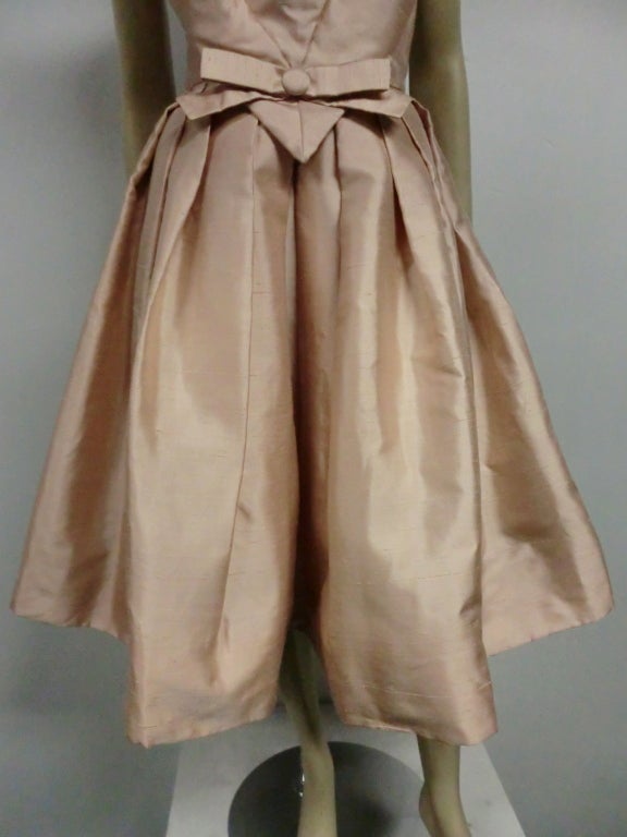 A 50s Paul Whitney silk shantung cocktail dress in pale pink with pleated skirt, built in crinoline and creatively structured bodice and open back detail.  Size 6-8