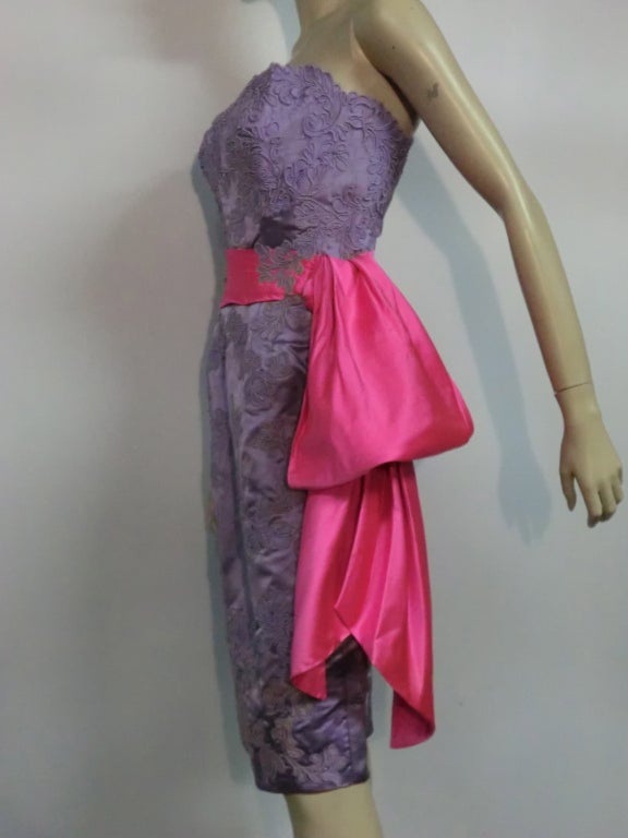 A fantastic and unusual 50s cocktail dress from Neiman Marcus.  Lavender silk satin appliquéd with delicate lilac lace and vivid fuchsia sash at the waist.  Structured and boned.  Never worn, but there is some minor color bleeding near hem.