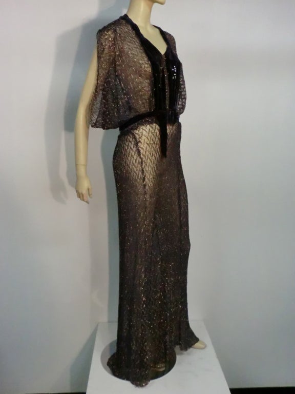 French quality metallic lace / mesh textile, in a heavier-than-usual weight, makes this 1930s gown flown beautifully! The color is aubergine with coin silver and it is trimmed with aubergine silk velvet and rhinestones. Grecian style draped short