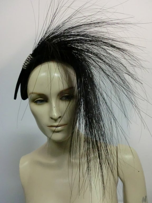 A fantastic 1950s G.Howard Hodge hat of black felt with a 1920s inspired look.  One size fits all bandeau style hat shape adorned with a huge spray of singed feathers and a rhinestone detail.  A real stunner!