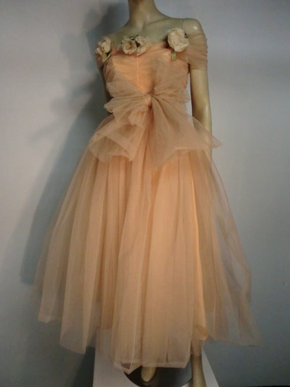 1950s Mary Carter peach tulle debutante party dress with a long wrap tie attached at shoulders which can be worn different ways!  We made a large bow at the waist in our photos.  Attached silk fabric flowers.  Boned and structured bodice with ruched