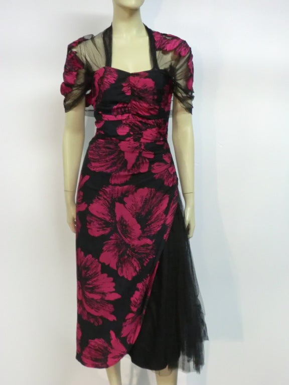 A gorgeous, vampy, sexy 1940s cocktail dress of rayon or silk crepe and tulle.  Large fuchsia hibiscus print gathered into a rouched bodice.  Silk tulle is gathered and radiates from one hip to hem.  Attached capelet is appliquéd with hibiscus print