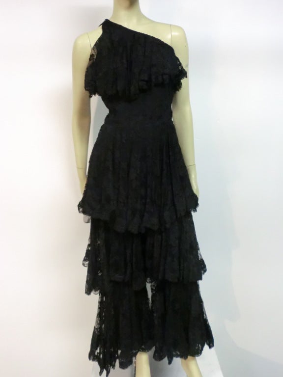 A fabulous 60s Donald Brooks design:  Tiered black silk lace jumpsuit, one-shoulder bodice, fitted underneath with a lace ruffle at bust line.  The legs are lined with crepe and triple-tiered in silk lace.  Each layer of lace is edged in horsehair