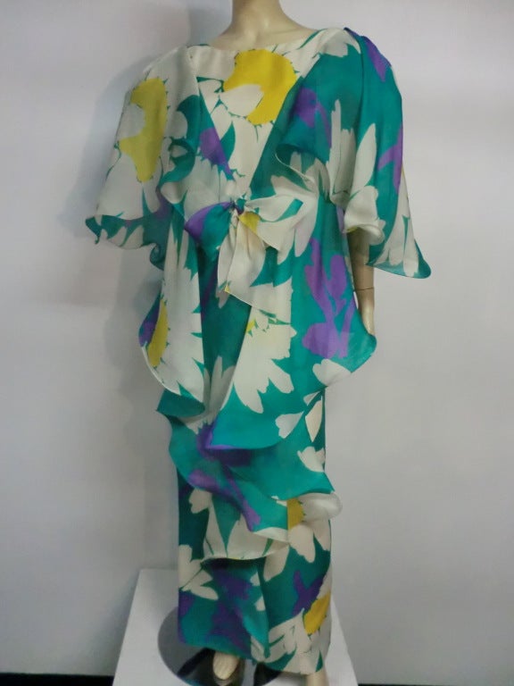 A fantastic, dramatic and bold 70s print silk organza large-scale floral daisy print in aqua, white, yellow and purple.  Large flutter shoulder cape treatment has horsehair braid underneath to give it maximum movement. Zippered at back. Bow at front.