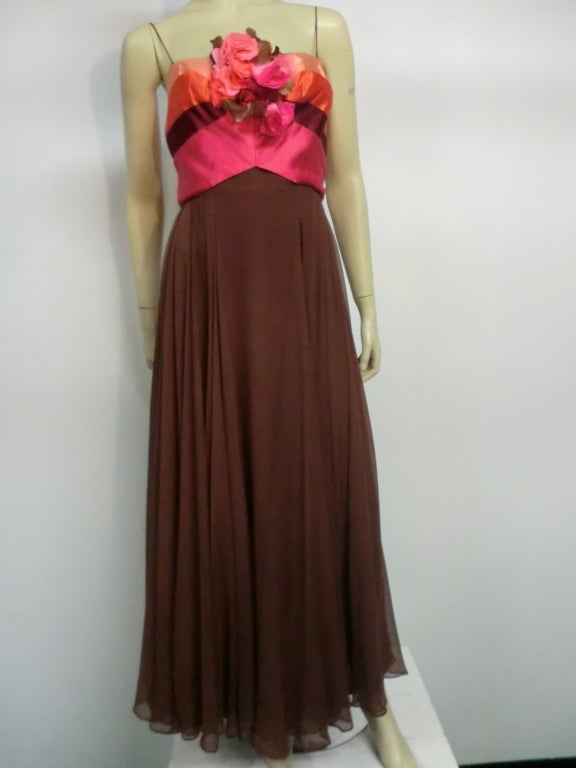 A gorgeous early 60s Helena Barbieri silk gown in mocha chiffon flowing double layered skirt and Empire bodice with vibrant silk satin bands in shades of apricot, fuchsia and peach.  Large spray of matching silk flowers at front.  Spaghetti straps. 