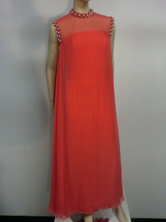 A beautiful 60s silk chiffon gown in vivid tomato red from Tee-ca.  Lined column-style underdress and floaty silk chiffon overlay.  Beaded trim embellishes the neckline and armholes.  Back zipper and buttons in overlay.