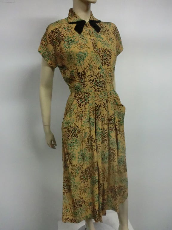 A fantastic 40s rayon crepe dress with hip pocket and velvet neck details.  A stylized foliage print in teal and black covers the a mustard gold background. Original belt not included.