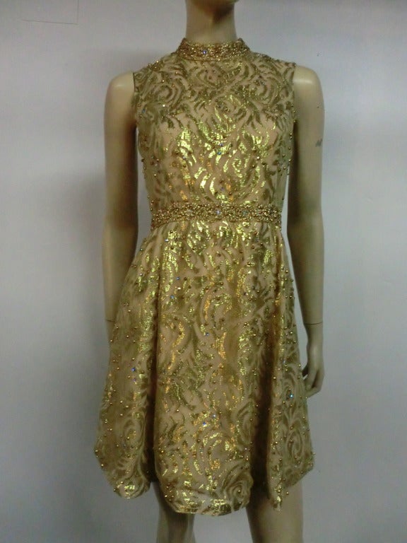 60s Mod baby doll dress:  In gold metallic lace with studs scattered throughout and braid trim at neck and waist.  Bodice fitted and flared mini skirt.  fully lined in beige fabric to create an illusion of sheerness.