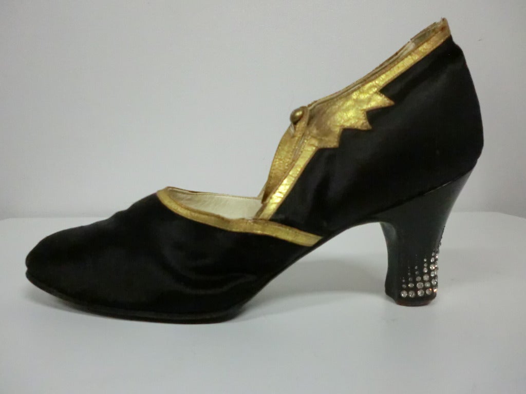 A gorgeous 1920's black peau de soi dancing shoe with gilt leather trim around the throat and ankle strap.  Button side closure.  Celluloid heel with 