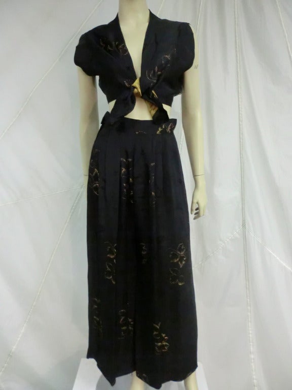 1940's black and gold woven rayon pajama set with smoking jacket.  Short sleeved pajama top snaps closed with a tie. Pants are high waisted with side closure and full leg. Smoking jacket has fitted waist with flared 