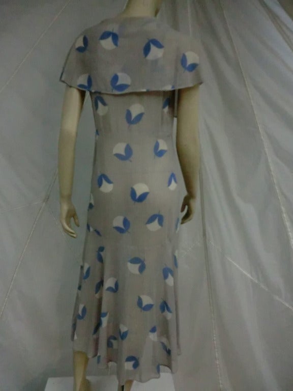 A sweet cotton voile day dress from the 20's/30's in gray with blue and white abstract flower print scattered throughout.  Front neckline ties and forms capelet.