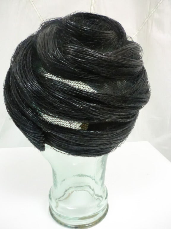A gorgeous, glossy black 1960's Christian Dior Chapeaux!  Set on a base of sheer silk mesh, ropes of black straw strands wind around the head in a beehive, turban fashion.  The straw ropes are enclosed in silk tulle to make it more durable and