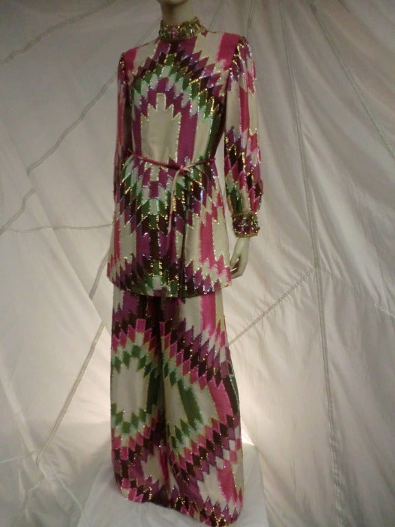 A fantastic 1960's Saks Fifth Avenue pantsuit in psychedelic patterned satin embellished with a banded jeweled collar and all-over sequin trim. Stove pipe leg pants with yolk at waist and belted tunic top.