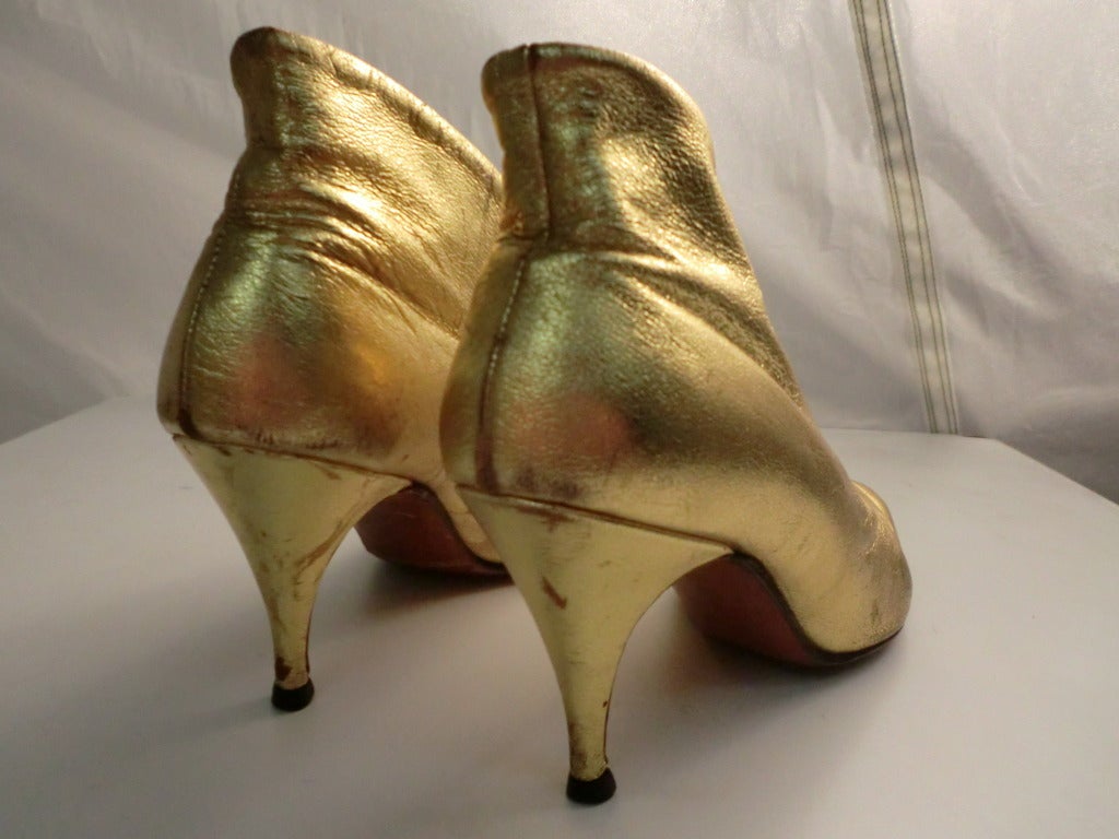 A fabulous pair of 1950s/1960s ankle booties with a plunging throat and stiletto heels.  Leather soles.  Wear to the gilding on leather throughout.