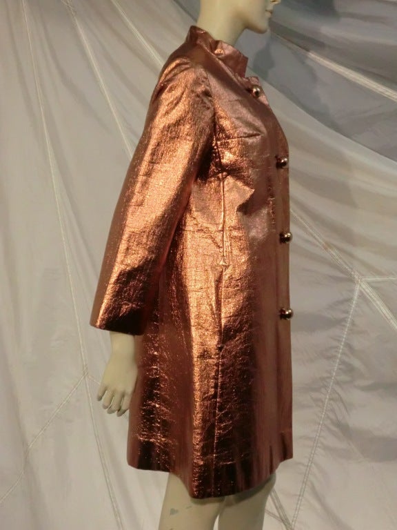 A wonderful 1960s Mod Saks Fifth Avenue faux leather raincoat in synthetic metallic copper foil, with spherical metallic buttons and original belt.  Nehru style collar.