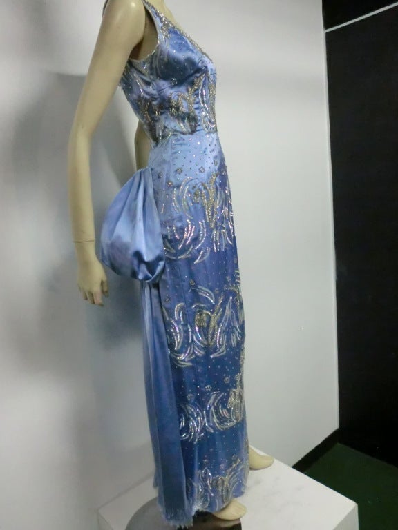 A gorgeous 1950s Christian Dior elaborately beaded and sequined ice blue silk satin fitted column gown with bustle-back in fringed silk satin. Beautiful stylized floral beading, prong-set rhinestones with fringed 