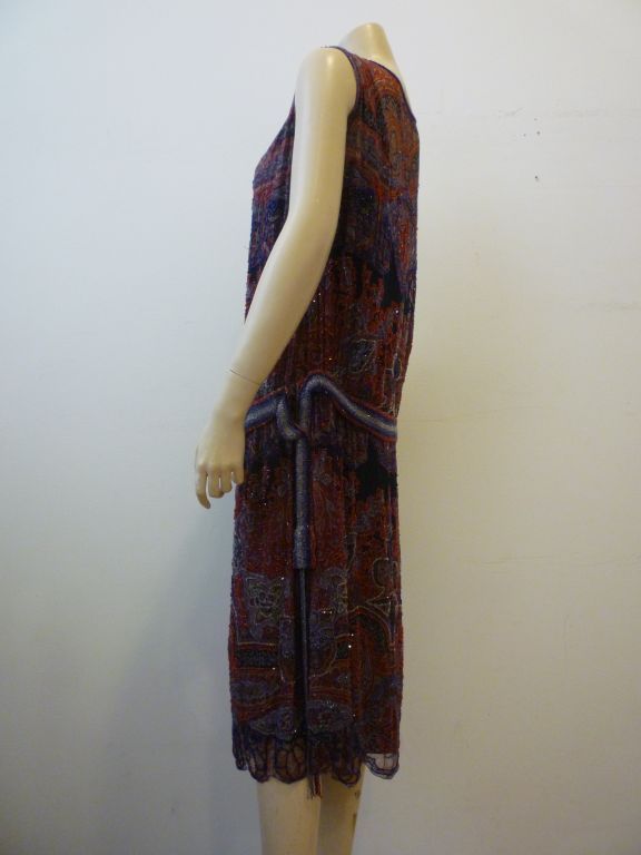 This is a beautiful 1920's paisley print silk chiffon knee-length drop-waist dress heavily beaded in colored beads corresponding to the silk print. Scalloped hem and beaded original belt included. In wonderful shape!