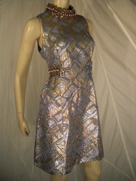 A stunning 1960s metallic brocade cocktail dress in pewter, silver and gold with a fitted bodice and a-line skirt.  Jeweled and beaded faux turtle neck and back belt.  Lined.