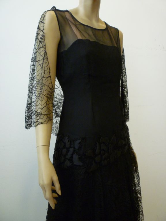 A fantastic 1920s cocktail dress for the liberated woman!  An easy chemise fit to the knee in black silk lace and chiffon.  An overlayer of fabric is padded and quilted in floral motif at the front hem! Wickedly modern!