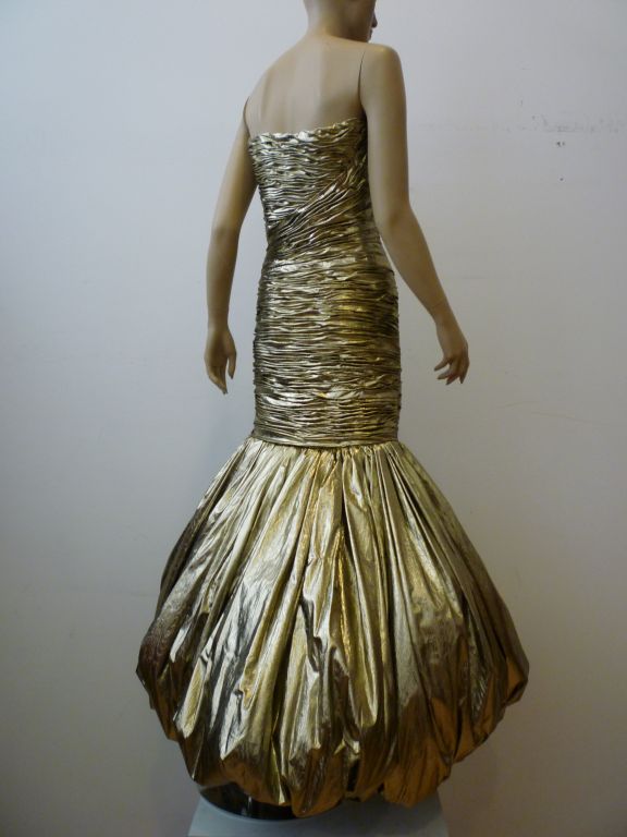 This is a real show stopper!  1980s gold lamé gown from Narakas - Parisis strapless and super-structured in the bodice, absolutely form-fitting down to the knee where it balloons to an extravagant bubble skirt! The height of bold 80s glamour!