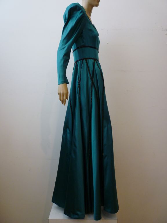 Gorgeous teal green silk satin 1970s Stavropoulos gown with low scoop neckline pleated full sleeves and graphic black glass beading. Crinoline under layer.