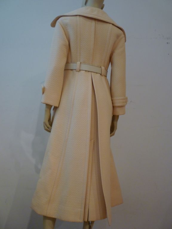 This smartly styled James Galanos for Amelia Grey trench style maxi-coat in cream textured wool with large notched lapels, button-flap patch pockets rear vent, comes with the original leather belt.  Approx. US size 6.