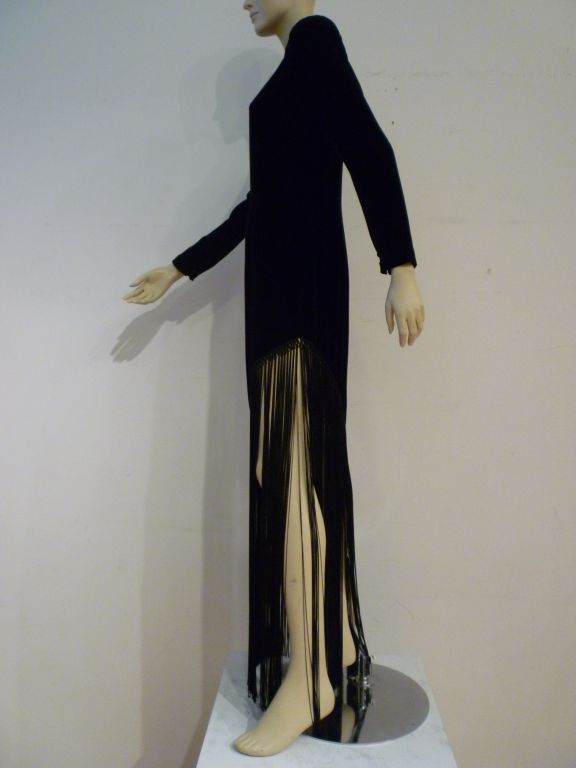 A dramatic 70s Bill Blass gown in imported black silk velvet with hand-knotted long long diagonally cut fringed hemline. Body is silk lined.  Sleeves have button and loop closures at wrist.  Hidden long back zipper.
