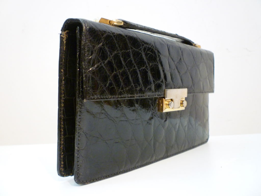 A distinctive strong business clutch in black alligator.  Made in France with gold tone hardware squeeze clasp and short strap.