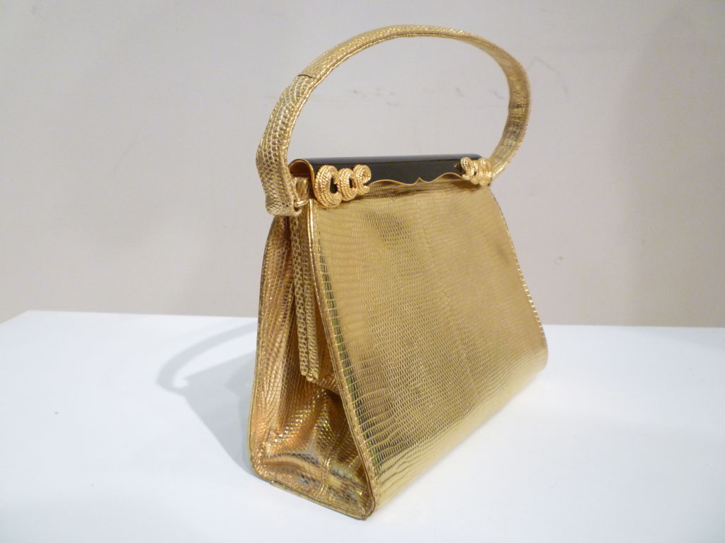 A spectacular 50s evening bag from Saks Fifth Avenue constructed of gold gilt lizard skin. Features black enameled spring-hinge closure embellished with gold metal scroll work.  Lined with beige satin, very clean. <br />
<br />
Dimensions: <br
