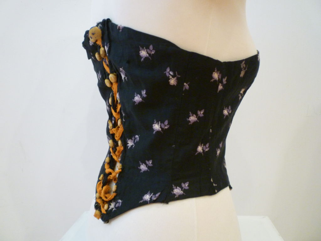 1880s silk corset cover in black cotton with purple floral pattern and lace up detail.  Waist measures 28-29.  12