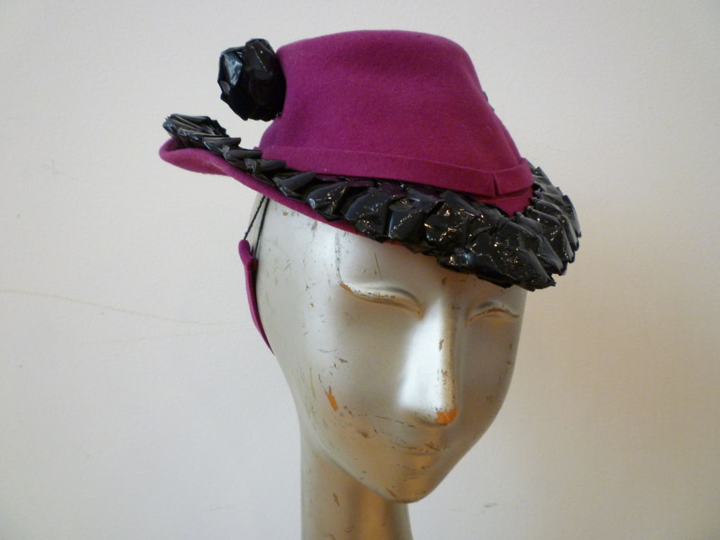This wonderful 40s fuchsia wool tilt hat with strap to be worn in back of head.  Trimmed in midnight blue braided cellophane.  One size fits all! Gorgeous!
