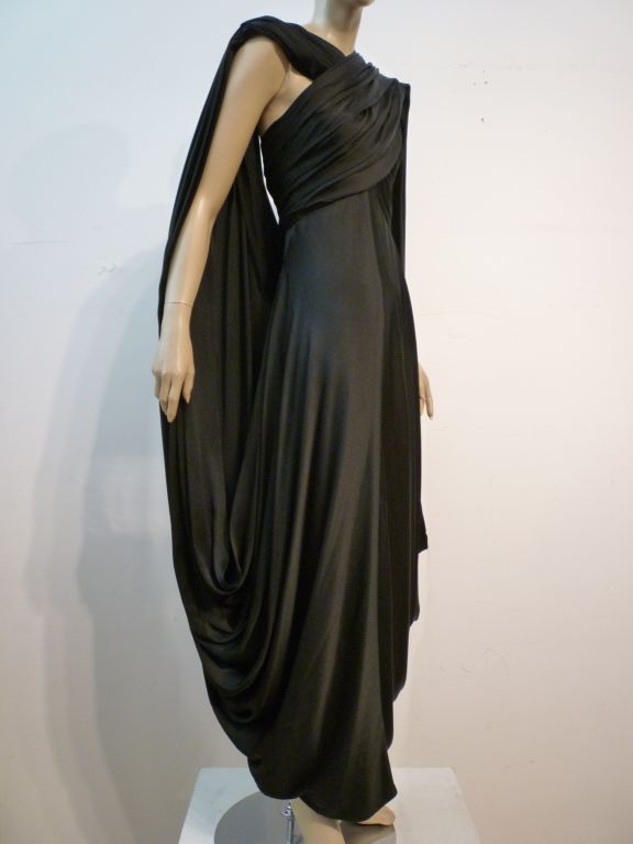 This dramatic black silk charmeuse Jacqueline de Ribes gown is spectacular with it's ruched and cross-draped bodice that loops around in back to join shoulder and skirt in a gorgeous cape that will make for an awe inspiring exit!  <br />
<br