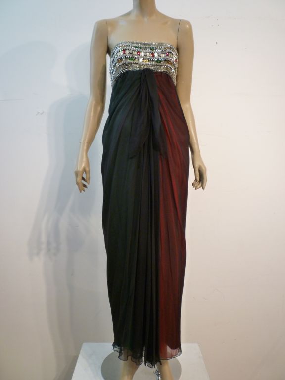 This incredible Galanos gown from 1965 is featured in the Galanos Retrospective book. The strapless bodice is heavily beaded and stoned with gold, red, green and clear stones and beads of various sizes and designs. The double layered skirt of the