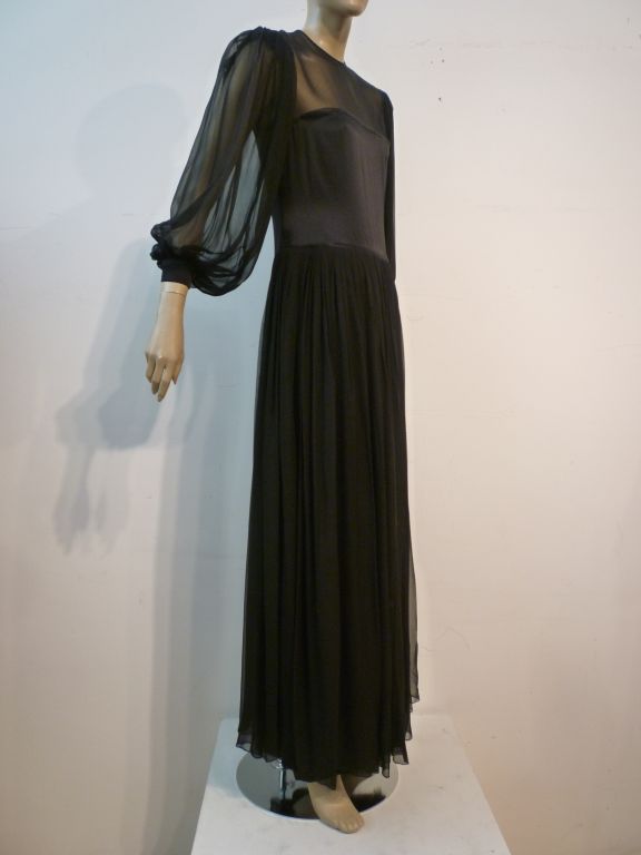 A beautiful and feminine James Galanos evening gown in beautiful black silk chiffon and satin with demure yet sexy sheer panels at decolletage, balloon sleeves and skirt...but with unexpected deep slits at the leg for plenty of sex appeal when