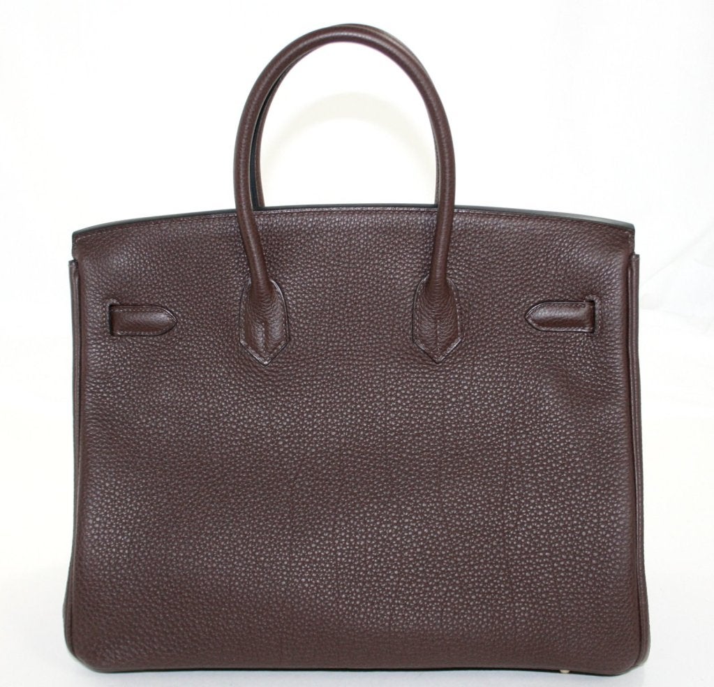 This authentic Hermès 35 cm Chocolate Togo Leather Birkin is in pristine condition, never before carried.  It has the protective plastic intact on the hardware and has been carefully stored.     Considered the ultimate luxury item the world over and