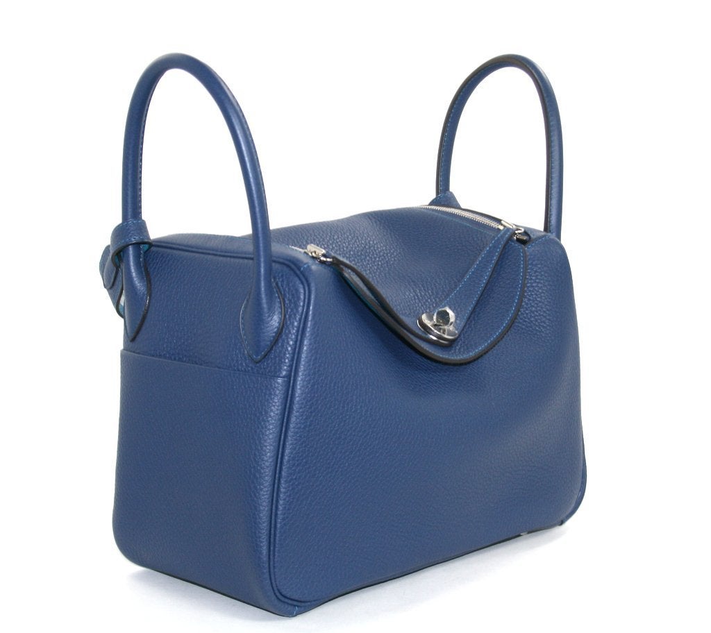 This authentic Hermès Blue Sapphire 30 cm Lindy is in pristine unworn condition.  A more relaxed alternative to the Birkin or Kelly, this Lindy is crafted in serene Blue Sapphire Clemence leather with a striking Blue Izmir interior.   Stitched by