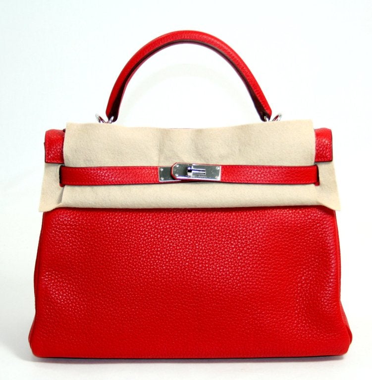 This Authentic Hermès Rouge Casaque Clemence 32 cm Kelly is in pristine unworn condition with the plastic intact on the hardware.   Hermès bags are considered the ultimate luxury item worldwide.  Each piece is handcrafted with waitlists that can
