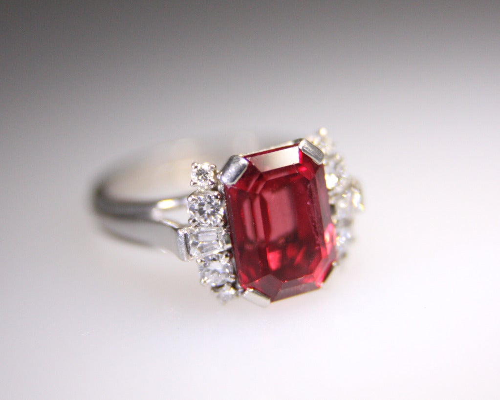 The ring made by Gubelin has a red emerald cut spinel weighing approximately 5.50 carats. It is further set with 8 round and 2 baguette-cut diamonds. Mounted in Palladium. Size 6 1/2.  Can be sized.