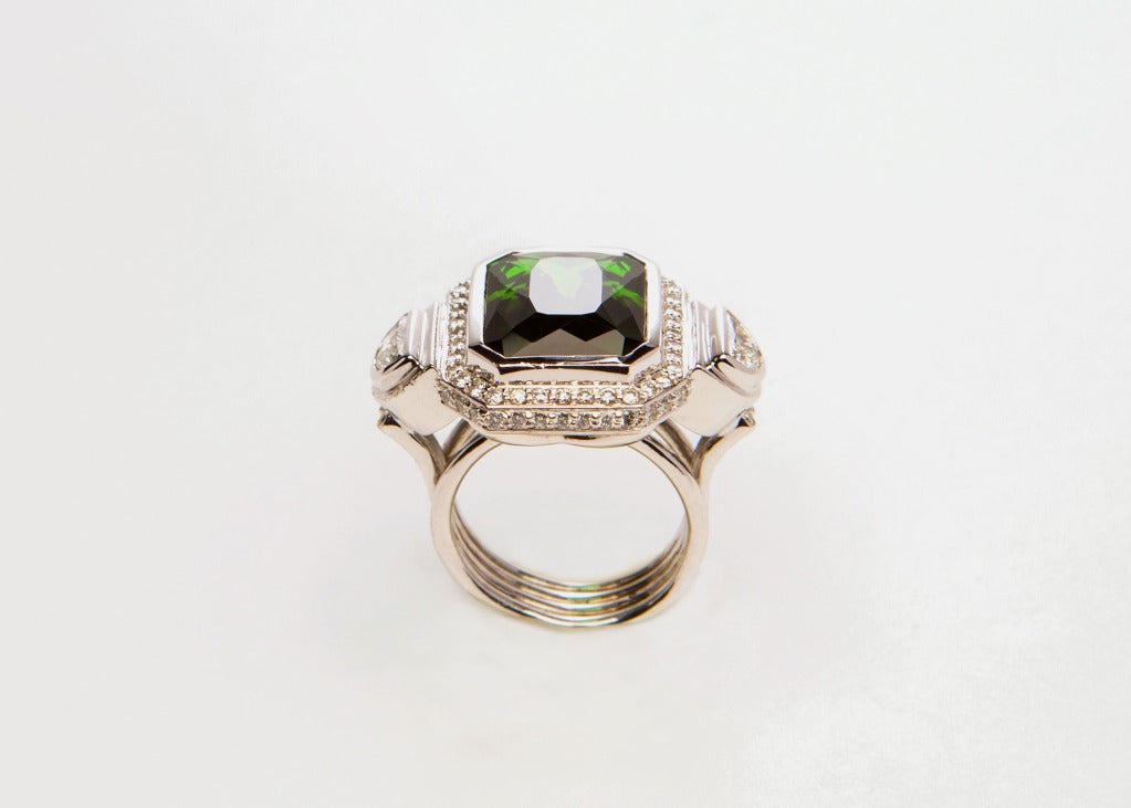 A vivid green 10 carat tourmaline is flanked by two half moon shaped diamonds.  This bold mounting is finished with brilliant cut diamonds created by Sam Lehr.