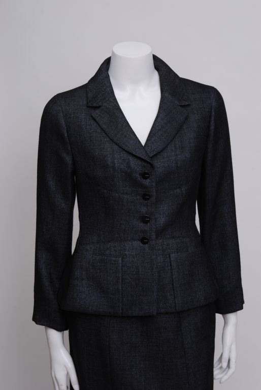 Chanel lightweight charcoal grey wool/silk blend skirt suit. Fabric has a slight metallic sheen. Chanel detail on buttons. Jacket weighted with silver metal chain. 

Chanel

Gabriel Bonheur (a.k.a. Coco Chanel) 19 August 1883-1971 

Coco