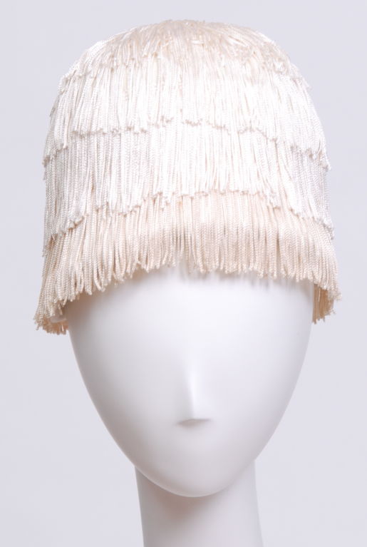Early 1960s, iconic Yves Saint Laurent fringe hat.  Four tiers of fringe, three upper being ivory and bottom being cream, attached to a cream wool felt, cloche base.  