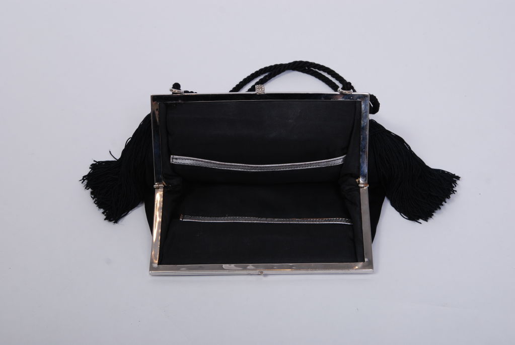 Shiny, black double faced silk satin deco purse with silver metal frame. Decorated with black celluloid and rhinestone detail and two thick silk fringe tassels. Interior lined in silk with silver leather trim. Kept in mint condition.