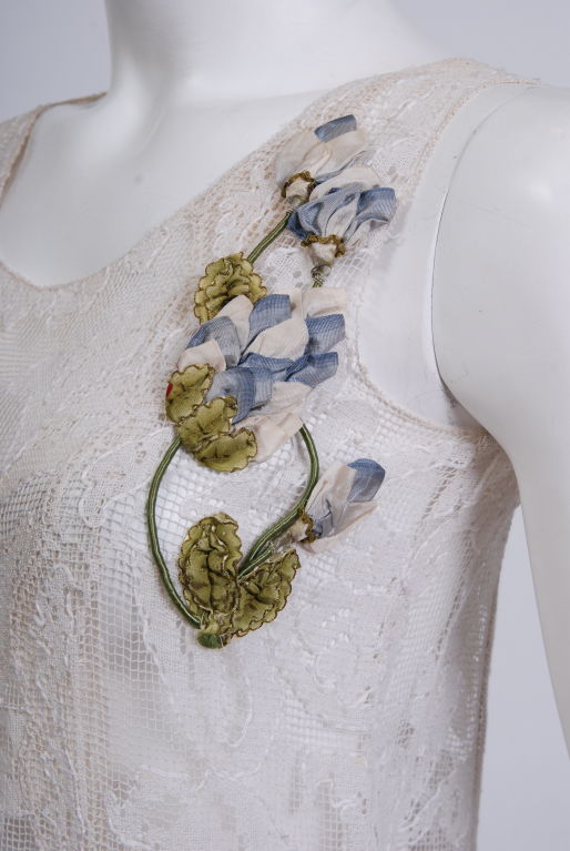French cotton and silk blend dress,sewn of hand made lace , with intricate embroidery woven throughout the pattern. Sleeveless with a simple flounce at the bottom. Ribbon appliqued floral corsage. Kept in pristine condition.