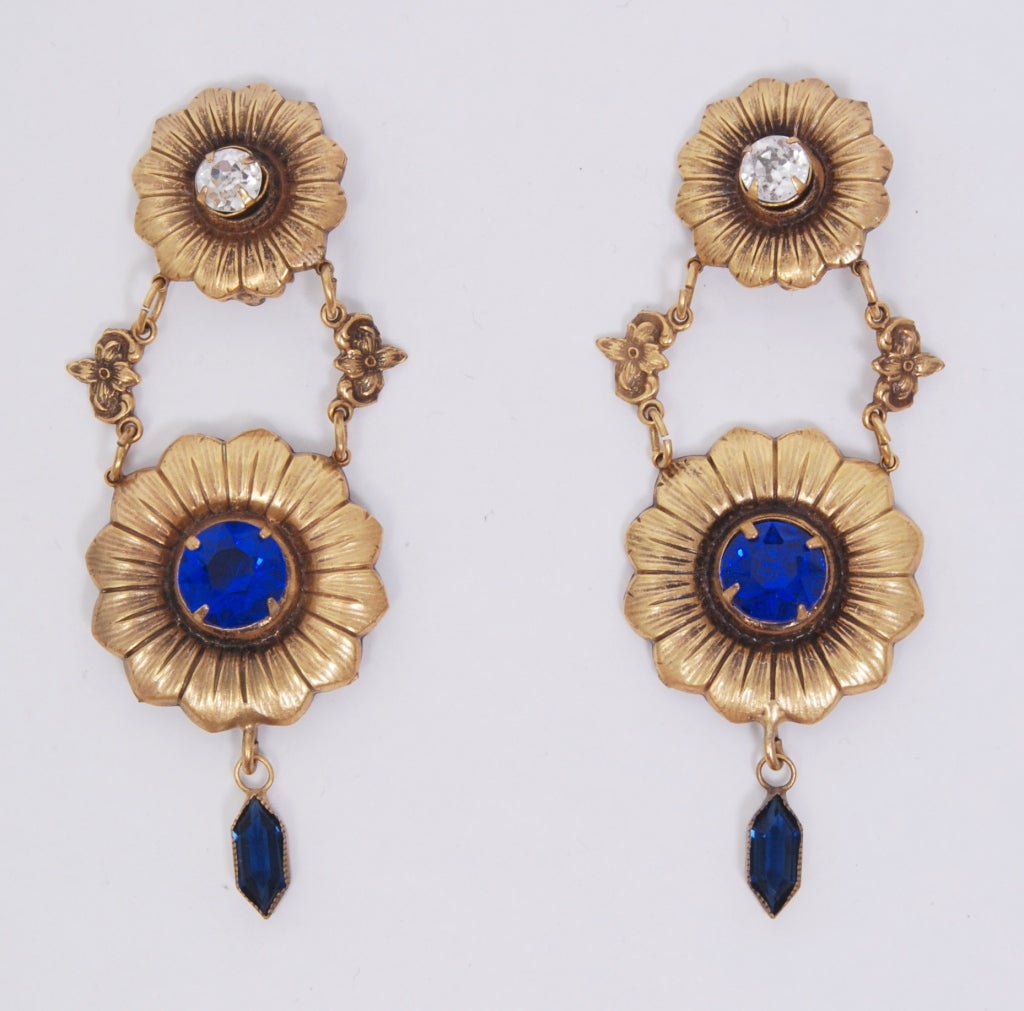 Unique drop clip earrings with a floral design, decorated with clear and royal blue crystal stones. Measures 3 inches long.