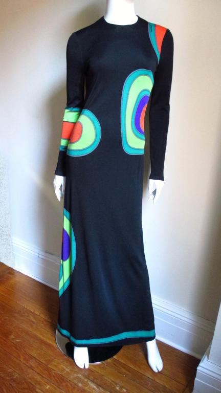 A full length long sleeved synthetic jersey dress by Louis Feraud with abstract shapes outlined in greens, orange and purple on a black background.  Long flattering dress skims the body and then flares slightly at the hemline.  Beautiful brightly